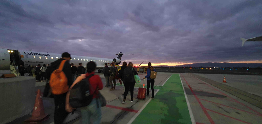 Fluggäste beim Einsteigen, im Hintergrund ein dramatischer Sonnenuntergang
